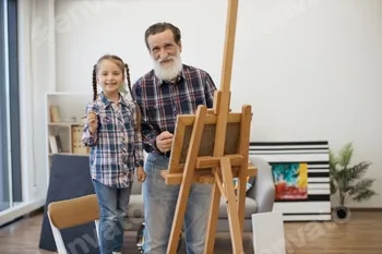 Older adult with girl posing behind easel with cloth in room