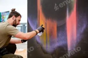 Attractive male artist is painting picture with paint spray can spraying it onto canvas