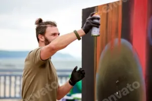 Attractive male artist is painting picture with paint spray can spraying it onto canvas