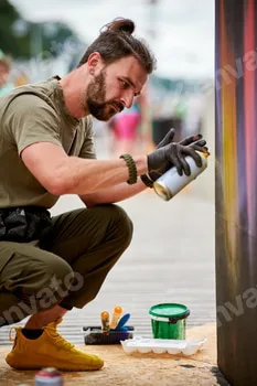 Attractive male artist is painting picture with paint spray can spraying it onto canvas