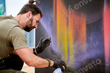 Attractive male artist is painting picture with paint spray can spraying it onto canvas