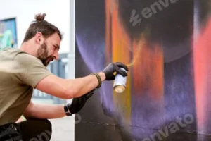 Attractive male artist is painting picture with paint spray can spraying it onto canvas