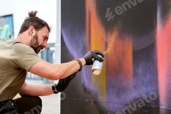 Attractive male artist is painting picture with paint spray can spraying it onto canvas