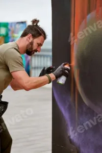 Attractive male artist is painting picture with paint spray can spraying it onto canvas