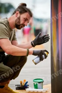 Attractive male artist is painting picture with paint spray can spraying it onto canvas