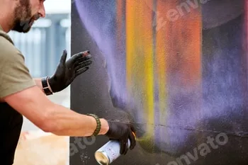 Attractive male artist is painting picture with paint spray can spraying it onto canvas