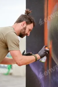 Attractive male artist is painting picture with paint spray can spraying it onto canvas