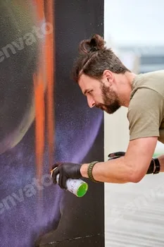 Attractive male artist is painting picture with paint spray can spraying it onto canvas
