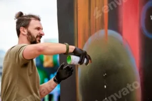 Attractive male artist is painting picture with paint spray can spraying it onto canvas