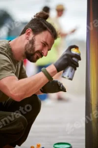 Attractive male artist is painting picture with paint spray can spraying it onto canvas