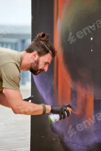 Attractive male artist is painting picture with paint spray can spraying it onto canvas