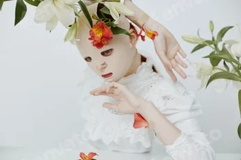 Surreal art portrait of a model with a mask and floral elements, expressing emotions of serenity and