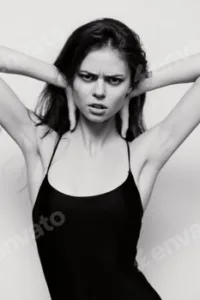 Intense expression of a young woman in a black outfit, hands holding her head, showcasing strong