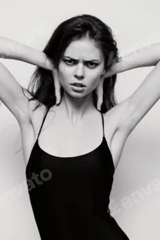 Intense expression of a young woman in a black outfit, hands holding her head, showcasing strong