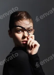 Stylish woman with fishnet veil posing elegantly against a dark background, showcasing contemporary