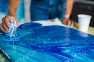 Person creating blue acrylic pour art on canvas. Art and creativity concept.