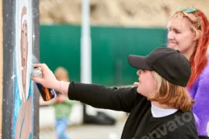 Two female artists painting picture with paint spray can spraying onto canvas at street exhibition