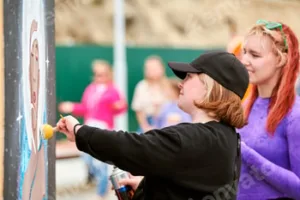 Two female artists painting picture with paint spray can spraying onto canvas at street exhibition
