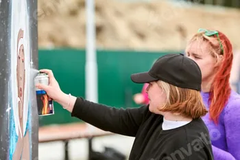 Two female artists painting picture with paint spray can spraying onto canvas at street exhibition