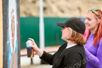 Two female artists painting picture with paint spray can spraying onto canvas at street exhibition